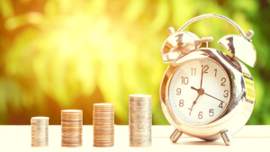 Previdência Privada e Suas Vantagens destaca na imagem montes de moedas simbolizando um gráfico com um relógio despertador no final do gráfico