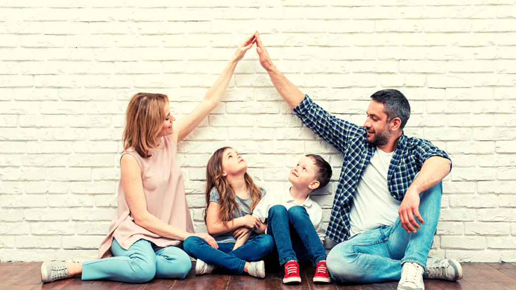 seguro de vida mostra Imagem de uma família com 4 pessoas e os pais fazendo uma proteção com as mãos sobre os filhos