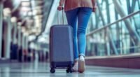 Como viajar mais e melhor em 2026 mostra uma mulher de costa no aeroporto levando uma mala de rodinha